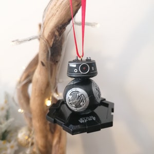 K&ouml;nnte beinhalten: Schwarzer und silberner Star Wars BB-8 Weihnachtsbaumschmuck mit einem roten Band, das an einem St&uuml;ck Treibholz h&auml;ngt.