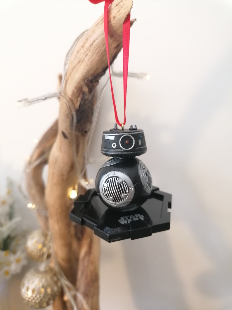 K&ouml;nnte beinhalten: Schwarzer und silberner Star Wars BB-8 Weihnachtsbaumschmuck mit einem roten Band, das an einem St&uuml;ck Treibholz h&auml;ngt.