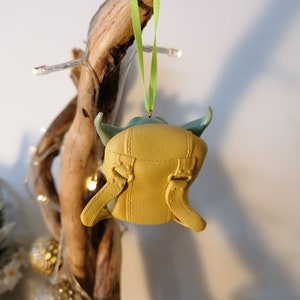 May include: A yellow and green Christmas ornament shaped like a character from the Star Wars franchise. The ornament is hanging from a green ribbon.