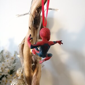 May include: A red and blue Spider-Man Christmas ornament hanging from a piece of driftwood with white lights wrapped around it.