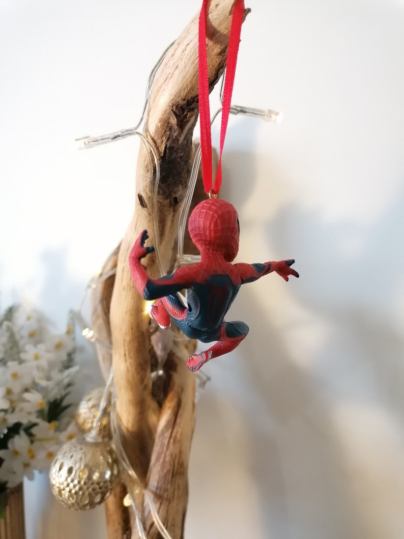 May include: A red and blue Spider-Man Christmas ornament hanging from a piece of driftwood with white lights wrapped around it.