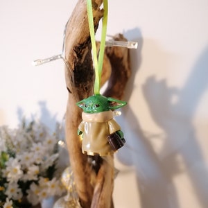 May include: A green and brown Yoda ornament with a green ribbon hanging from a piece of driftwood.