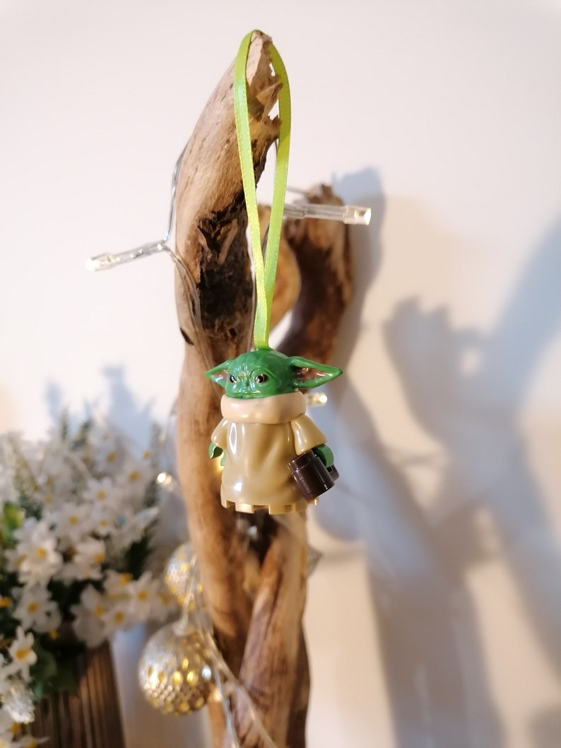 May include: A green and brown Yoda ornament with a green ribbon hanging from a piece of driftwood.