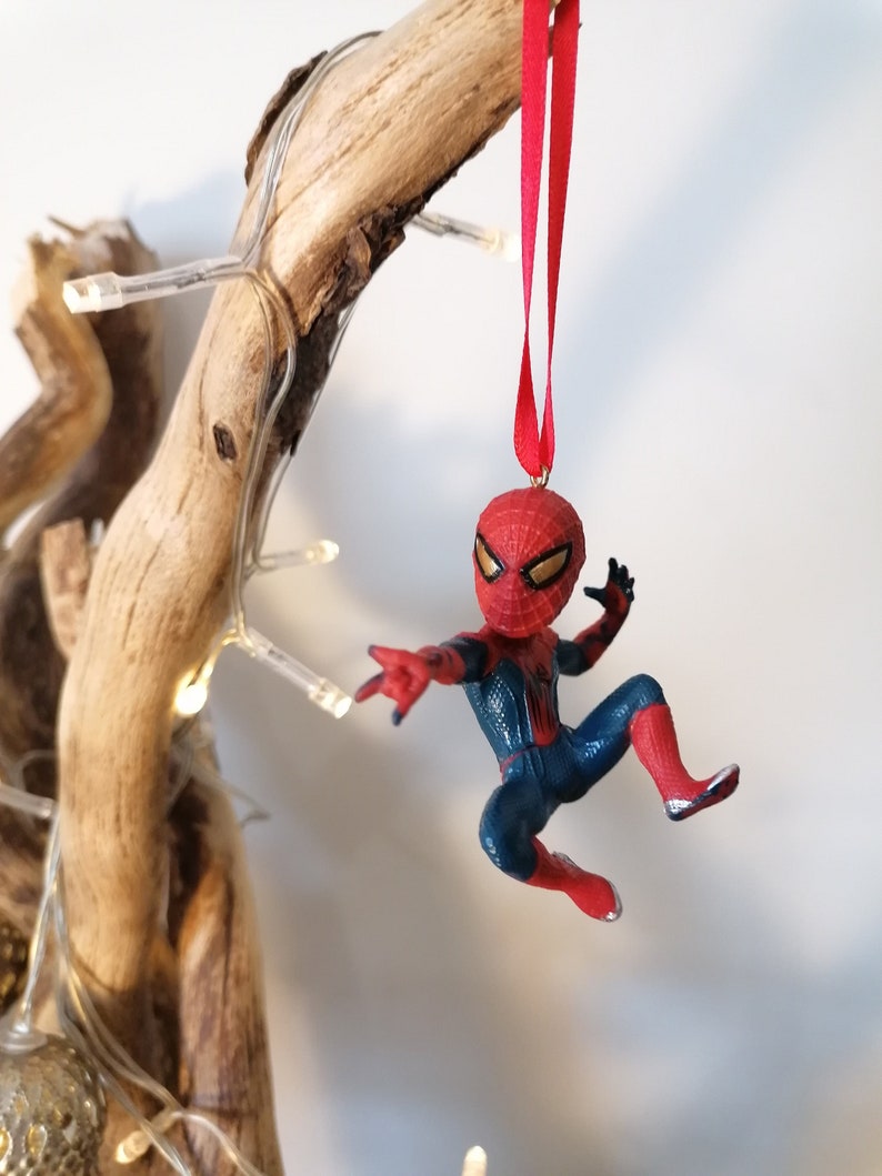 May include: A red and blue Spider-Man Christmas ornament hanging from a branch with a red ribbon.