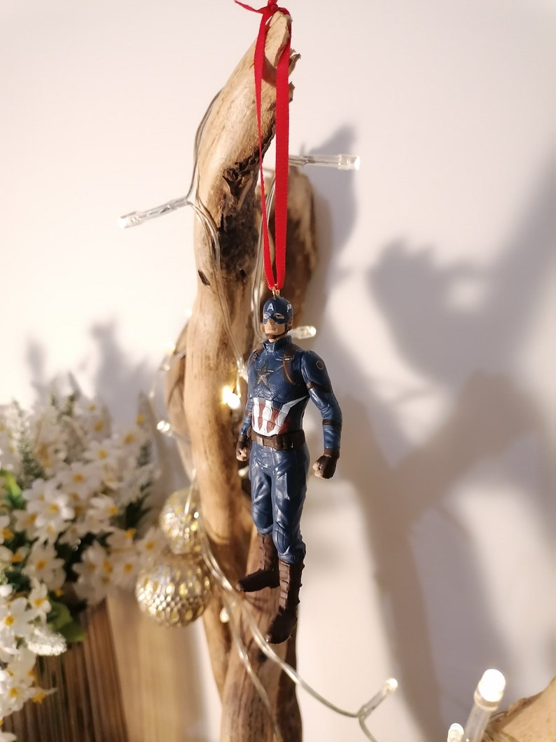 May include: A blue and red Captain America figurine ornament hanging from a red ribbon on a piece of driftwood.