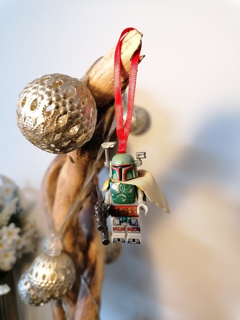 May include: A green and brown Lego Star Wars Boba Fett minifigure ornament with a red ribbon hanging from a piece of driftwood.