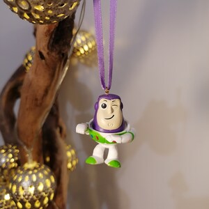 May include: Purple and white plastic figurine of Buzz Lightyear from the Toy Story franchise. The figurine is wearing a purple space ranger suit with a green vest and a white helmet. The figurine is winking and has a gold star on its chest.