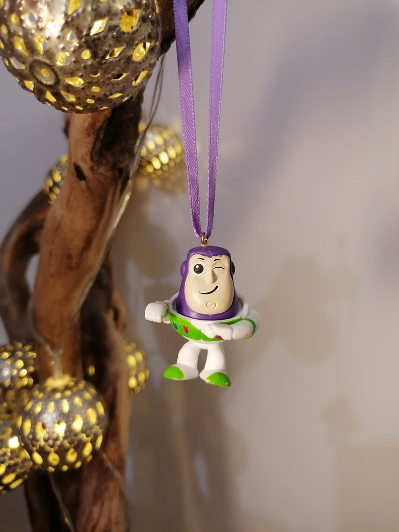May include: Purple and white plastic figurine of Buzz Lightyear from the Toy Story franchise. The figurine is wearing a purple space ranger suit with a green vest and a white helmet. The figurine is winking and has a gold star on its chest.