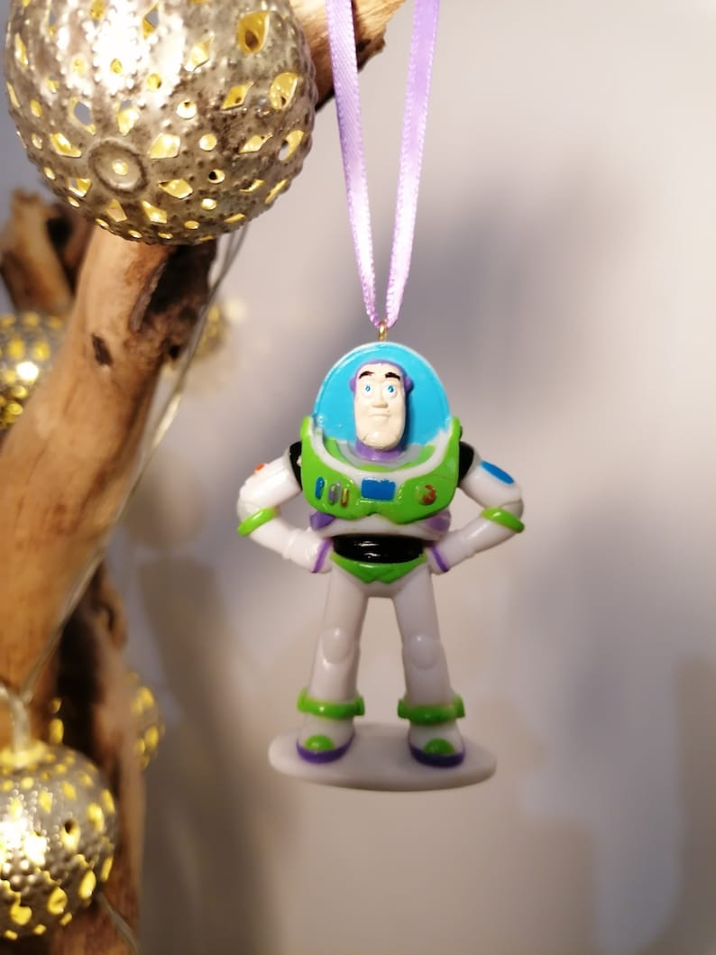 Puede incluir: Un adorno de pl&aacute;stico verde y blanco de Buzz Lightyear de la franquicia Toy Story. El adorno est&aacute; colgado de una cinta morada.