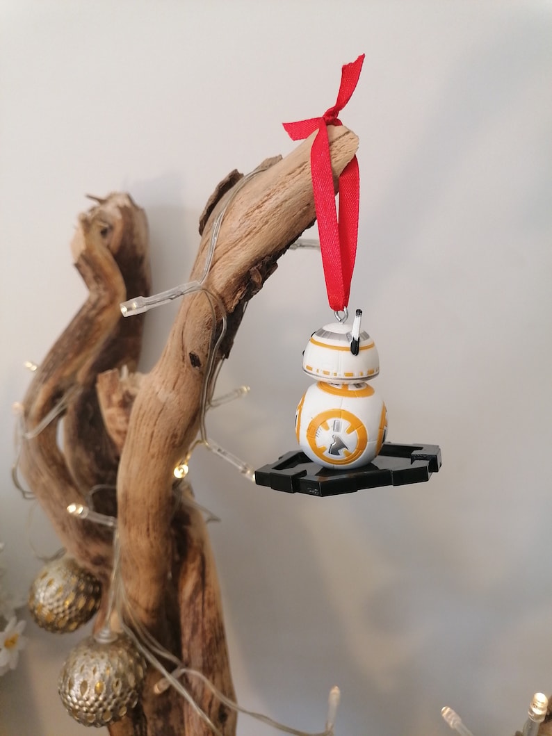 May include: A white and orange Star Wars BB-8 character Christmas bauble with a red ribbon hanging from a branch of driftwood.