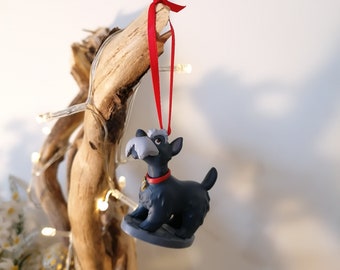 May include: A gray and black dog ornament with a red collar and a red ribbon hanging from a branch. The ornament is a Christmas decoration.