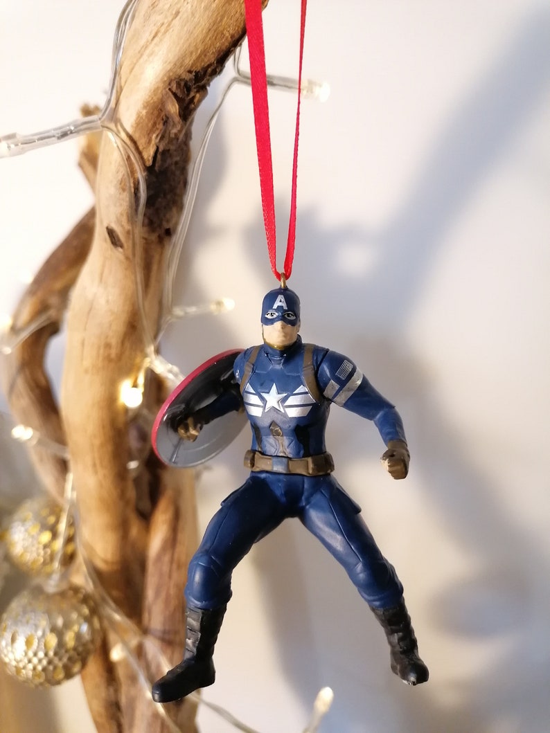 May include: A blue and red Captain America Christmas ornament with a red ribbon. The ornament features a detailed figure of Captain America holding his shield.