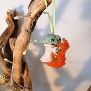 May include: A green and pink Christmas bauble featuring a character from the Star Wars franchise, holding a red and orange creature in its arms.