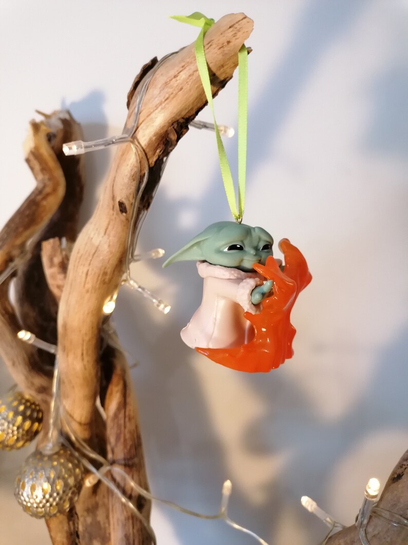 May include: A green and pink Christmas bauble featuring a character from the Star Wars franchise, holding a red and orange creature in its arms.