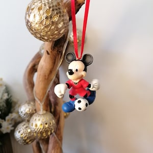 K&ouml;nnte beinhalten: Roter und wei&szlig;er Weihnachtsbaumschmuck mit Mickey Mouse als Fu&szlig;ballspieler, der einen Fu&szlig;ball h&auml;lt. Der Schmuck h&auml;ngt an einem roten Band.