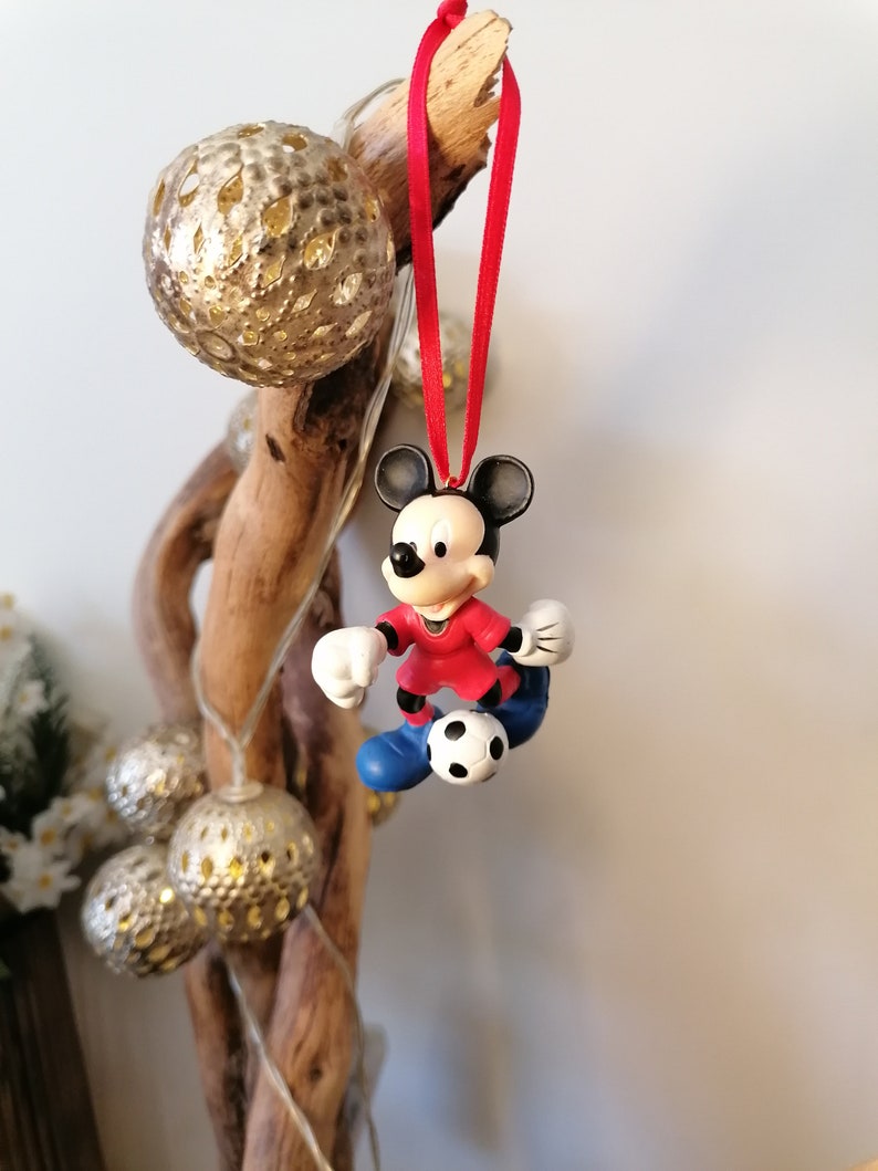K&ouml;nnte beinhalten: Roter und wei&szlig;er Weihnachtsbaumschmuck mit Mickey Mouse als Fu&szlig;ballspieler, der einen Fu&szlig;ball h&auml;lt. Der Schmuck h&auml;ngt an einem roten Band.