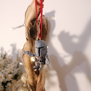 May include: A grey and white Star Wars character ornament with a red ribbon hanging from a piece of driftwood.
