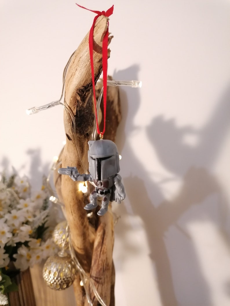 May include: A grey and white Star Wars character ornament with a red ribbon hanging from a piece of driftwood.
