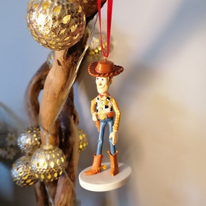Op de afbeelding: Een rode draad hangt aan een tak van hout met een witte basis en een klein plastic beeldje van Woody uit Toy Story. Woody draagt zijn kenmerkende cowboyhoed, vest en jeans.