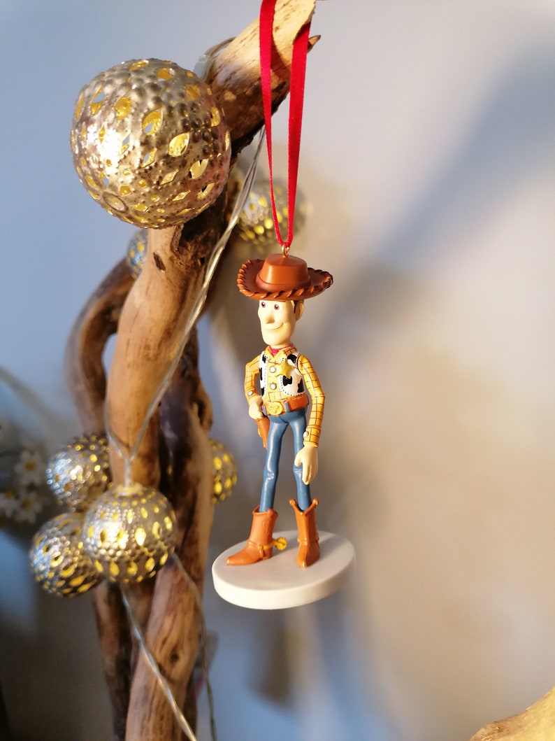 Op de afbeelding: Een rode draad hangt aan een tak van hout met een witte basis en een klein plastic beeldje van Woody uit Toy Story. Woody draagt zijn kenmerkende cowboyhoed, vest en jeans.