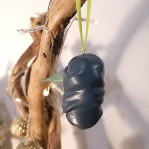 May include: A dark blue and green ceramic ornament with a textured surface, hanging from a green ribbon.