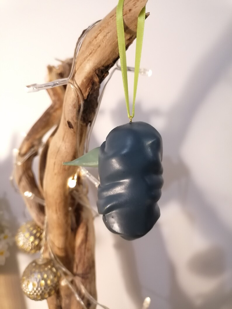 May include: A dark blue and green ceramic ornament with a textured surface, hanging from a green ribbon.