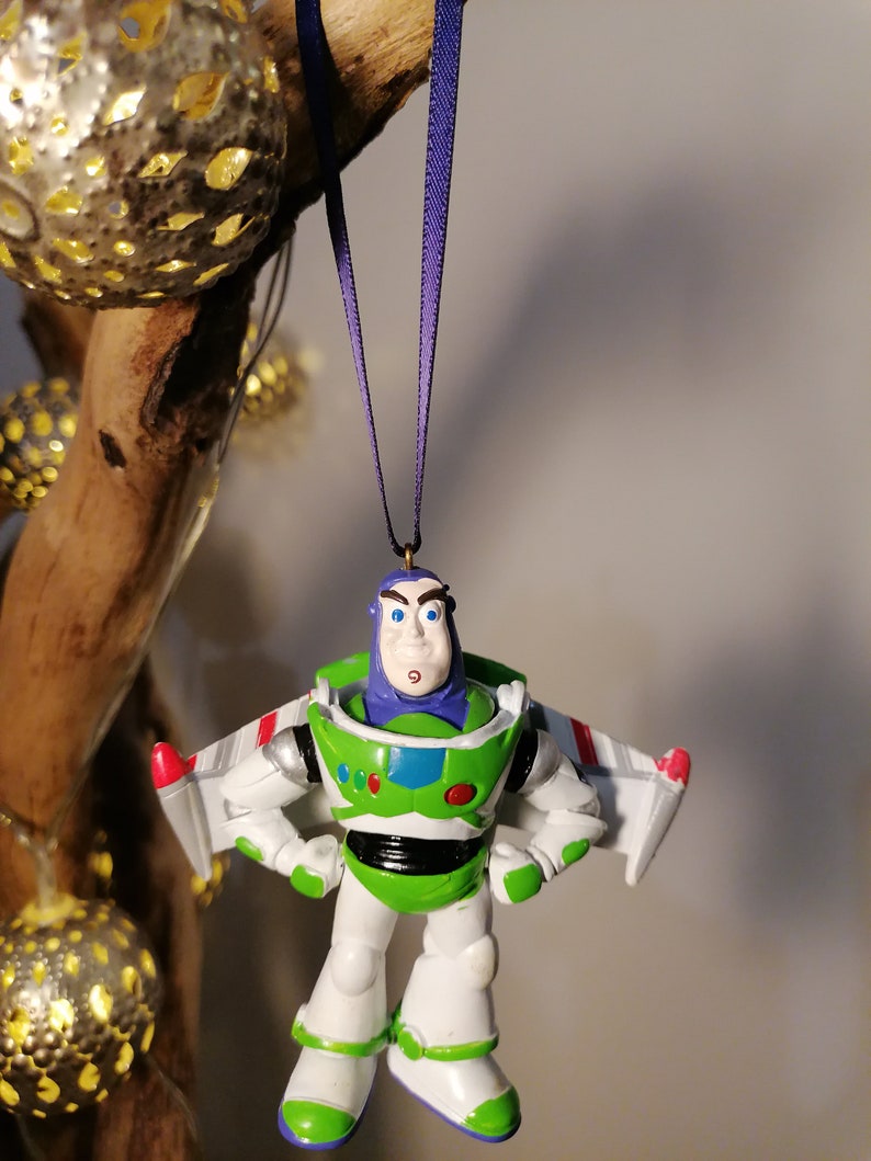 Pu&ograve; includere: Un ornamento di giocattolo in plastica verde e bianco di Buzz Lightyear del franchise Toy Story. L'ornamento &egrave; appeso a un nastro viola e presenta la tuta da ranger spaziale di Buzz Lightyear, il suo casco e le sue ali.