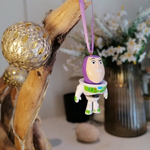 Puede incluir: Adorno de pl&aacute;stico morado y blanco de Buzz Lightyear de la franquicia de pel&iacute;culas Toy Story. El adorno est&aacute; colgado de una cinta morada.