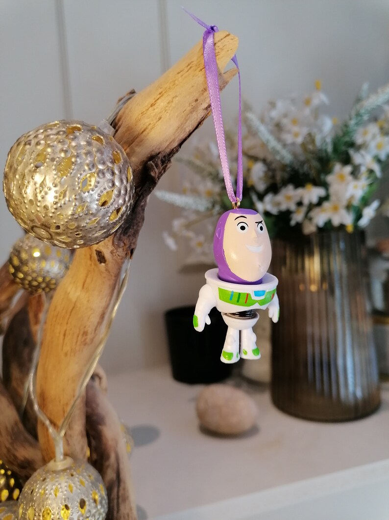 Puede incluir: Adorno de pl&aacute;stico morado y blanco de Buzz Lightyear de la franquicia de pel&iacute;culas Toy Story. El adorno est&aacute; colgado de una cinta morada.