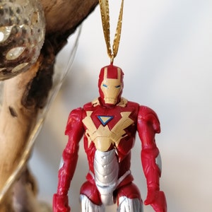 Pode incluir: Ornamento de figura de a&ccedil;&atilde;o do Homem de Ferro vermelho e prateado com uma fita dourada. A figura usa um traje vermelho e prateado com uma placa de peito amarela e uma viseira azul.