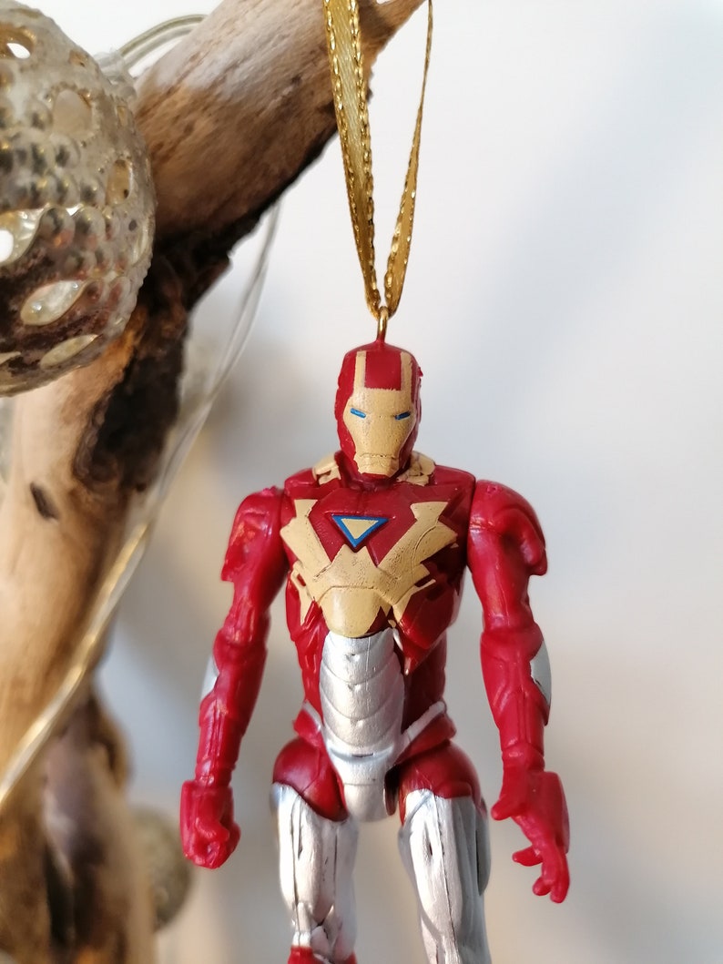 Pode incluir: Ornamento de figura de a&ccedil;&atilde;o do Homem de Ferro vermelho e prateado com uma fita dourada. A figura usa um traje vermelho e prateado com uma placa de peito amarela e uma viseira azul.