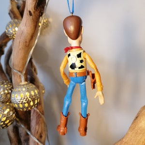 Puede incluir: Una figura de juguete de pl&aacute;stico de Woody de la franquicia de pel&iacute;culas Toy Story. La figura lleva su chaleco marr&oacute;n, sus vaqueros azules y su sombrero de vaquero caracter&iacute;sticos. Est&aacute; colgado de una cinta azul.
