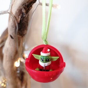 Pu&ograve; includere: Un addobbo natalizio rosso con una figura Lego verde e bianca di Baby Yoda che indossa un cappello da Babbo Natale.