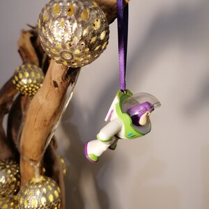 May include: A purple and green Buzz Lightyear Christmas ornament hanging from a branch with gold and silver ornaments.