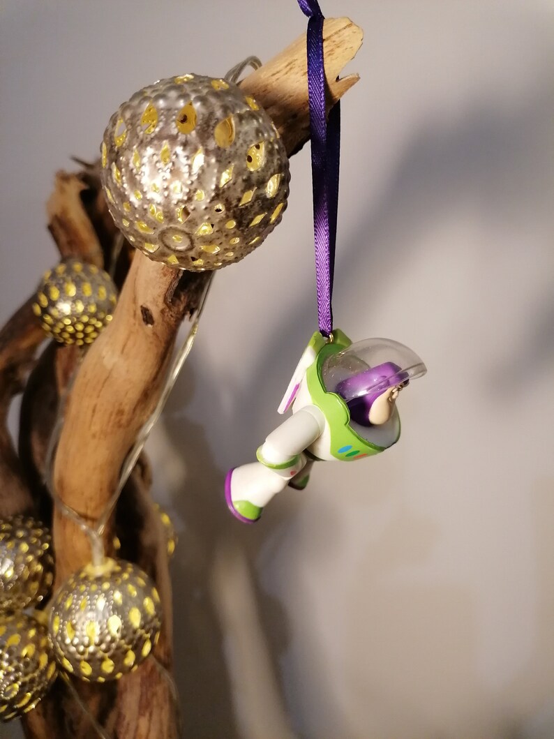 May include: A purple and green Buzz Lightyear Christmas ornament hanging from a branch with gold and silver ornaments.