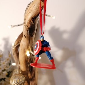 May include: A red, white, and blue Captain America Christmas ornament. The ornament features Captain America standing on a red surfboard, holding his shield.