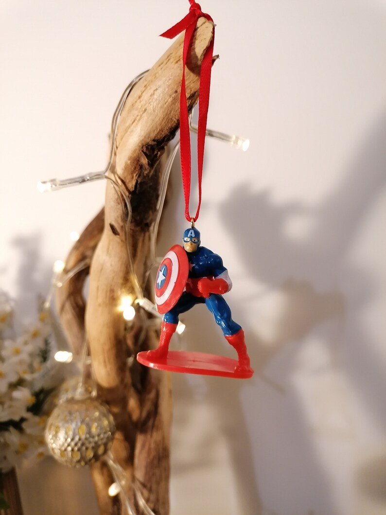 May include: A red, white, and blue Captain America Christmas ornament. The ornament features Captain America standing on a red surfboard, holding his shield.