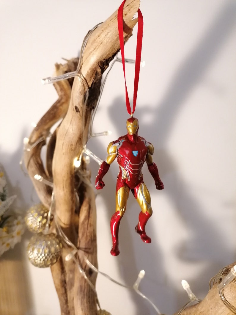 May include: Red and gold Iron Man Christmas ornament hanging from a branch with white lights.