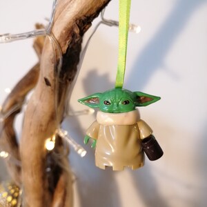 May include: A green and brown Yoda ornament with a green ribbon hanging from a branch. The ornament is holding a small brown cup.