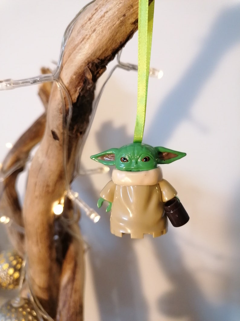 May include: A green and brown Yoda ornament with a green ribbon hanging from a branch. The ornament is holding a small brown cup.