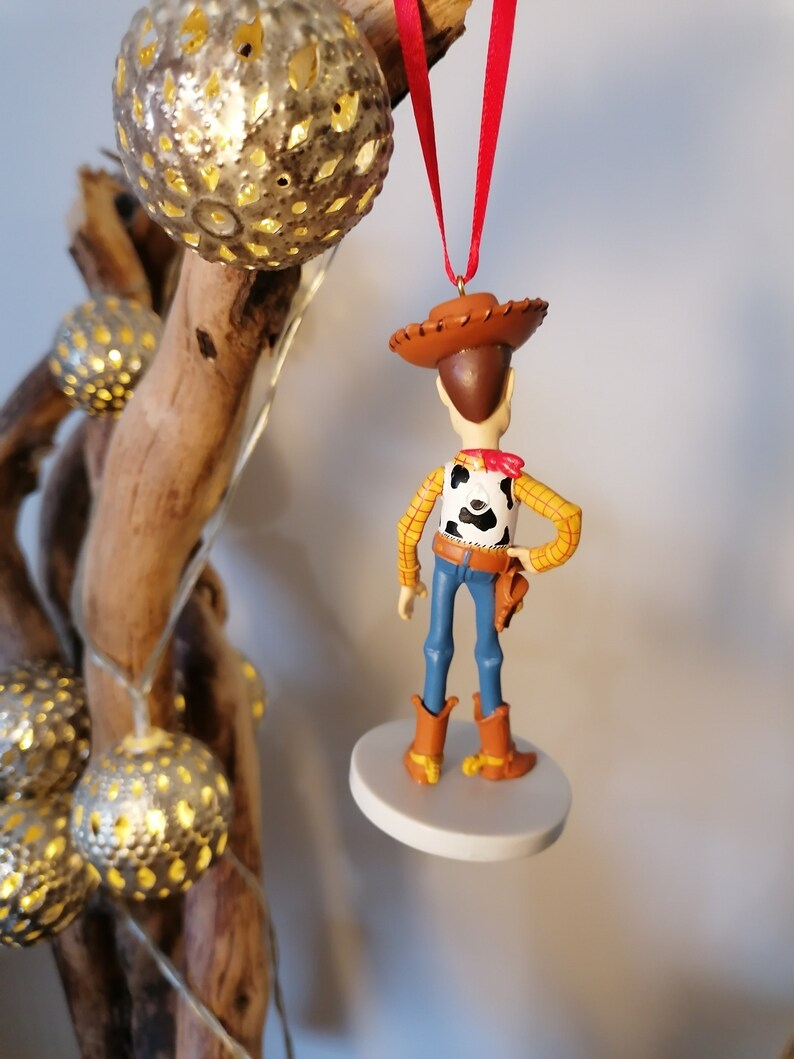 Op de afbeelding: Een rode draad hangt aan een witte ronde basis met een klein plastic beeldje van Woody uit Toy Story. Woody draagt zijn kenmerkende cowboyhoed, vest en jeans. Hij staat met zijn rug naar de camera.