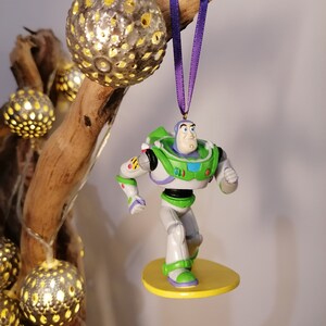 K&ouml;nnte beinhalten: Eine gr&uuml;ne und wei&szlig;e Plastikfigur von Buzz Lightyear aus der Toy Story-Reihe. Er steht auf einem gelben Surfbrett mit einem lila Band, das an seinem Kopf befestigt ist.