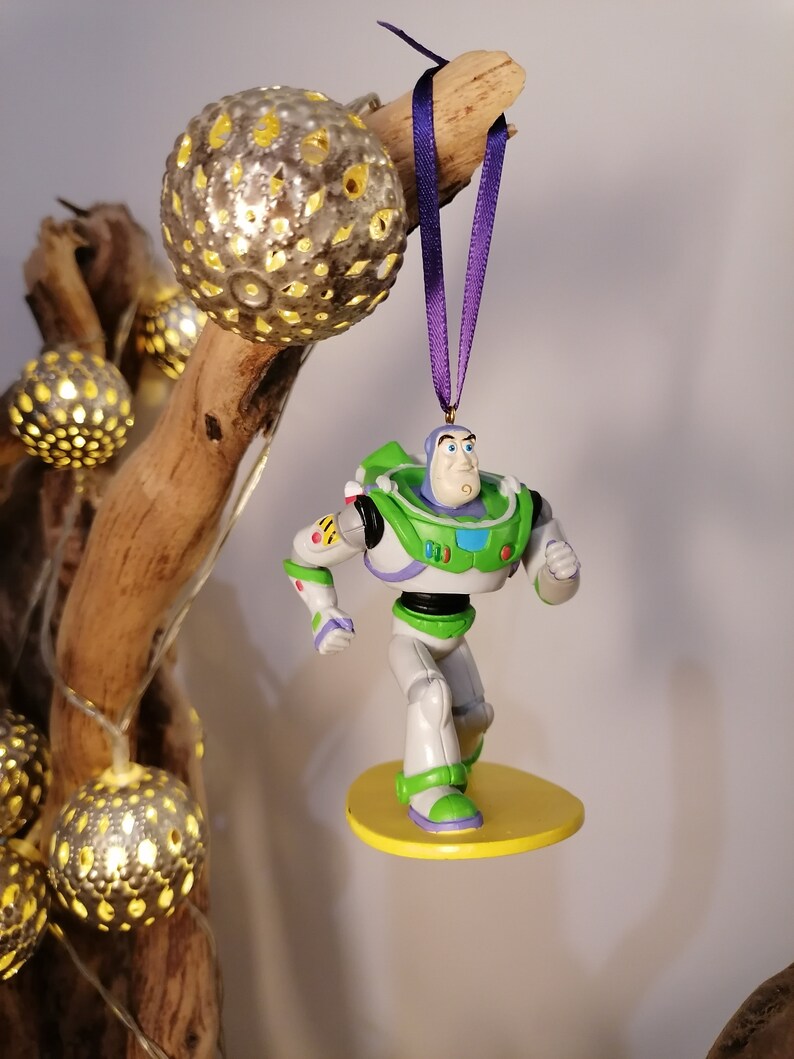 K&ouml;nnte beinhalten: Eine gr&uuml;ne und wei&szlig;e Plastikfigur von Buzz Lightyear aus der Toy Story-Reihe. Er steht auf einem gelben Surfbrett mit einem lila Band, das an seinem Kopf befestigt ist.
