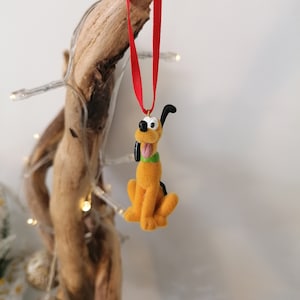 May include: A plush orange and brown dog ornament with black ears and a green collar. The ornament is hanging from a red ribbon.