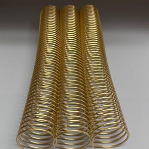 May include: Three gold metal binding coils, each with multiple loops, are arranged side by side on a gray surface.