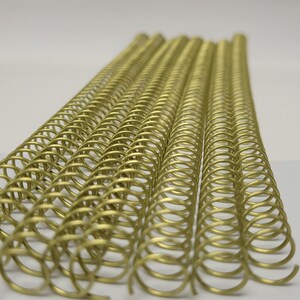 May include: A close-up of multiple gold metal binding coils. The coils are arranged in rows and are ready to be used for binding documents.