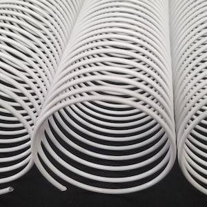 May include: Three white plastic coil binding spines, each with multiple loops, are arranged side-by-side on a black surface.