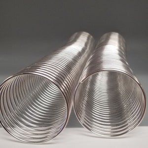 May include: Two silver metal coils, each made of multiple rings, are stacked on top of each other. The coils are shiny and reflect light.