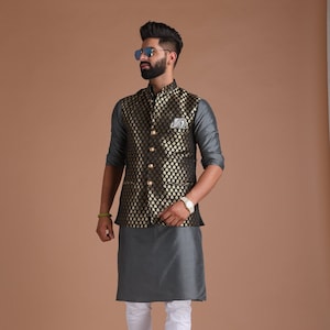 以下が含まれることがあります： グレーのクルタと白いパンツを組み合わせたフォーマルな装い。黒と金の模様のベストがアクセント。黒いブーツとポケットチーフが、スタイリッシュでまとまりのあるルックを演出しています。