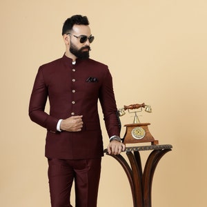 May include: A maroon suit with a mandarin collar and button closures. The suit is worn by a person with a beard and sunglasses. The person is standing next to a wooden table with a vintage phone on it.